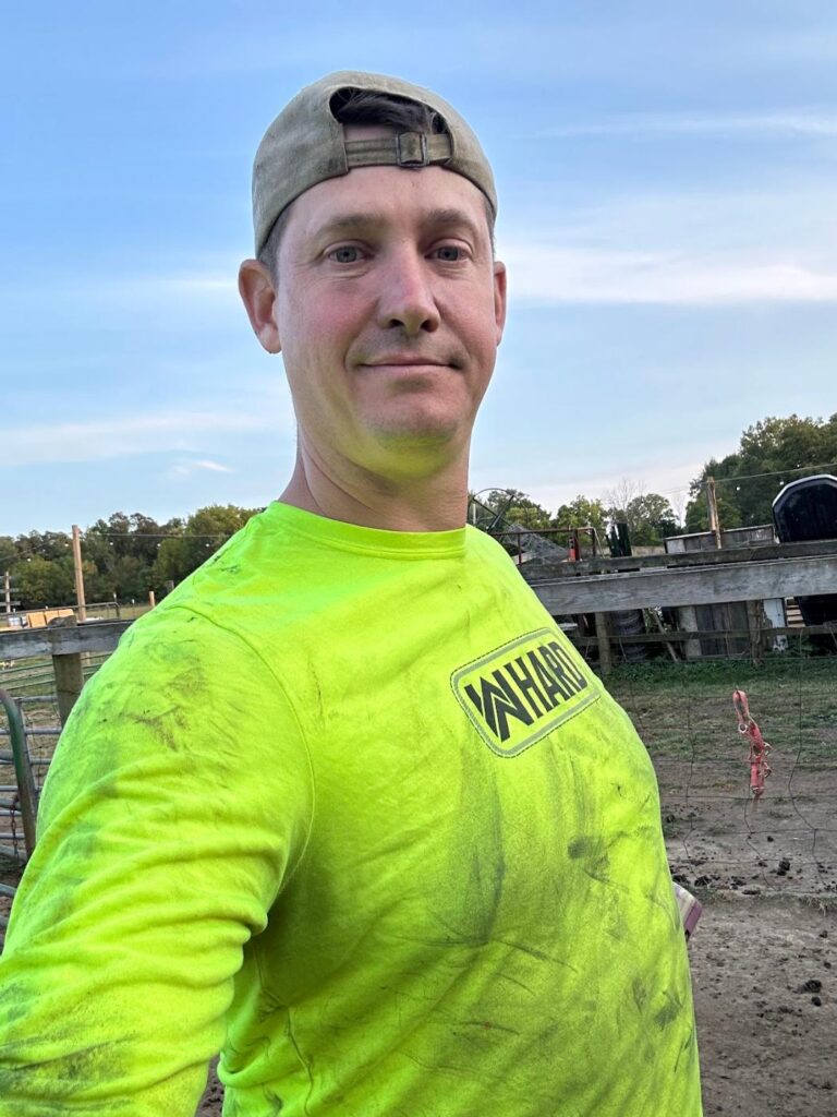 Phil Ratcliff in a muddy work shirt and cap at the farm paddock