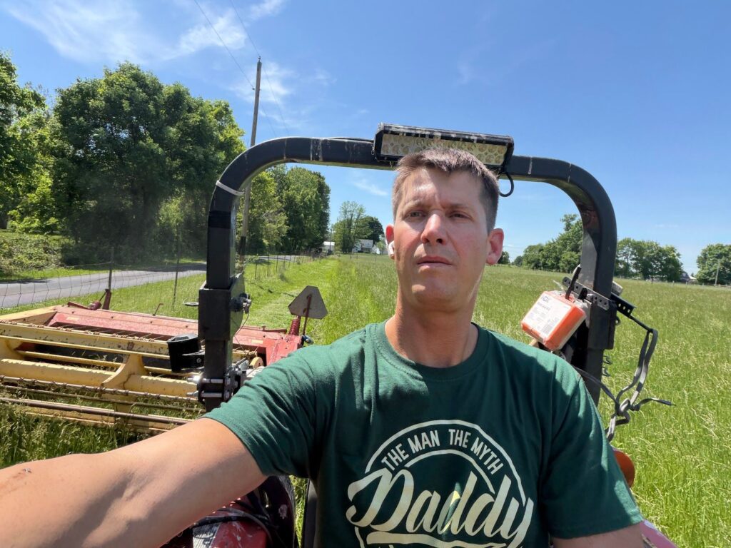Phil Ratcliff on his tractor mowing hay on a sunny day