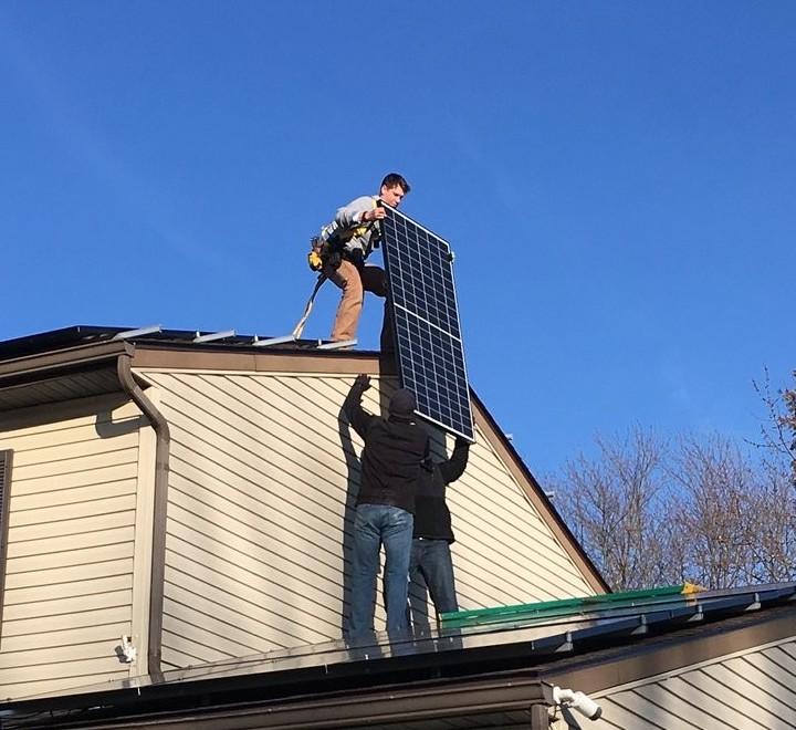 Phil up top on the roof taking a solar panel handed up from below